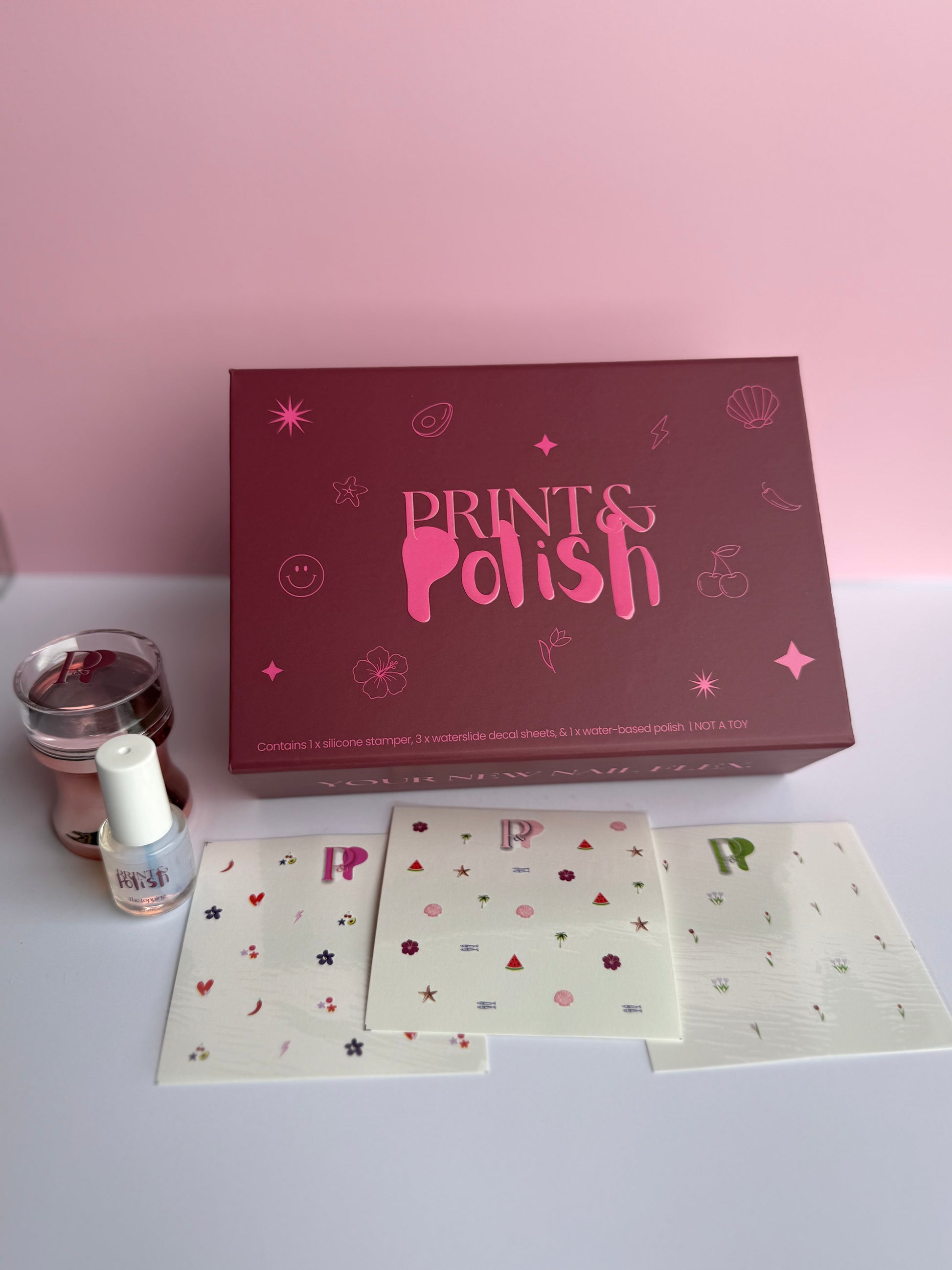 Prints & Polish nail art kit with box, cards, and nail polish on a light pink background