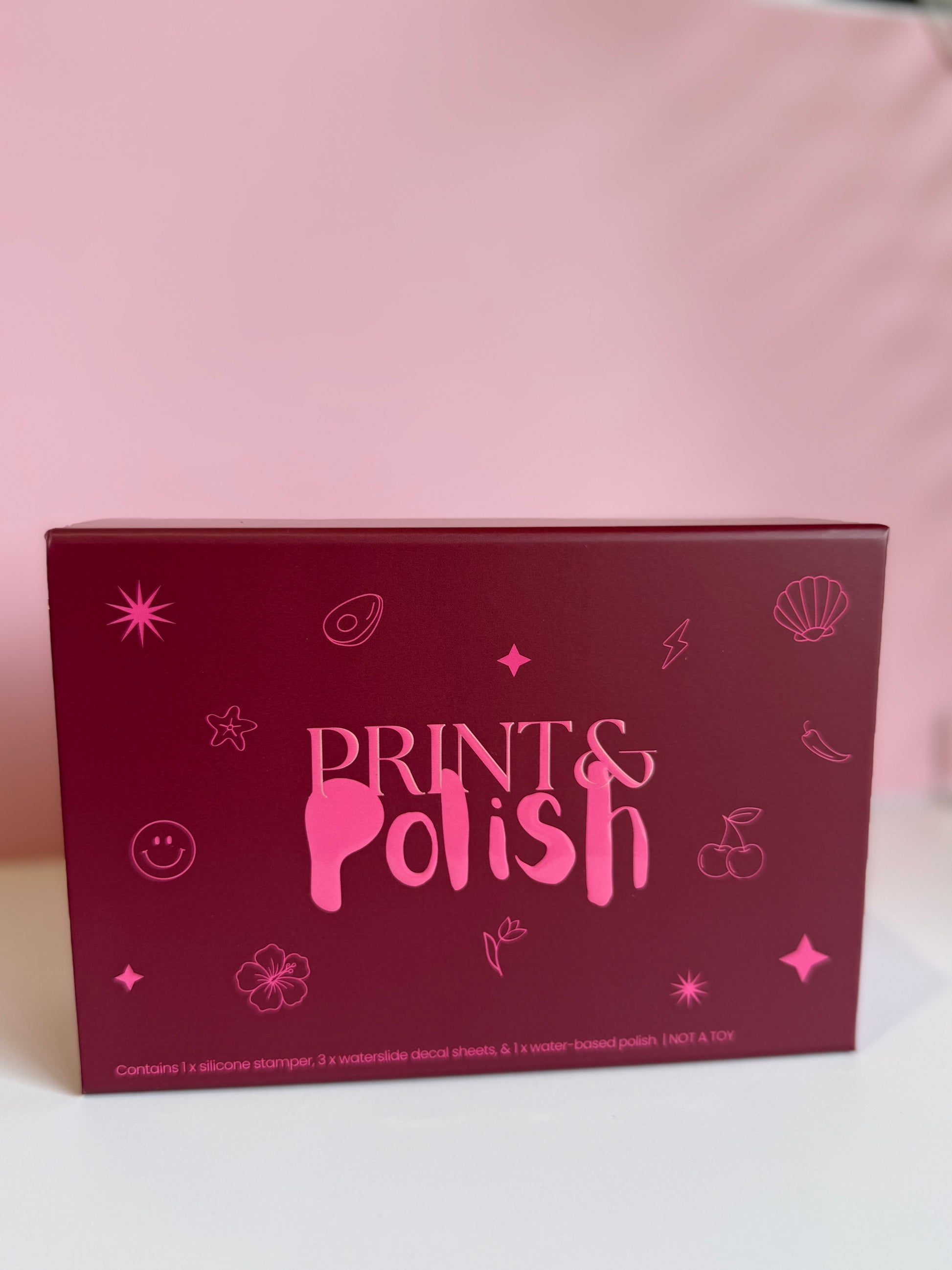 Pink 'Prints & Polish' product packaging on a light pink background